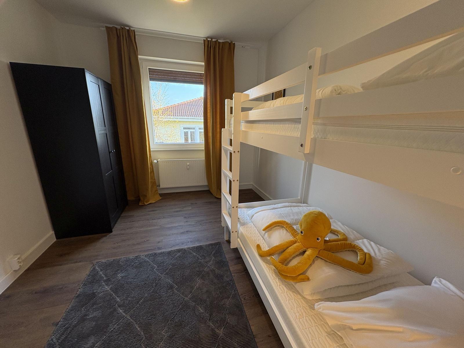 Zimmer mit Doppelstockbett, Fenster, Kleiderschrank und Teppich