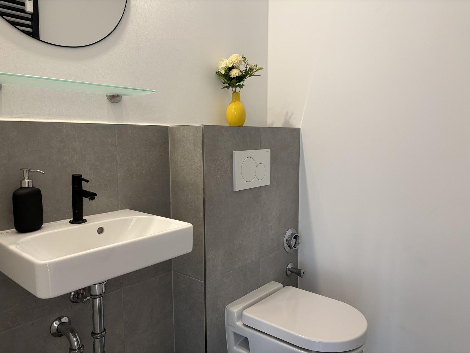 Badezimmer mit Waschbecken, Toilette und gelbem Vasenblumenarrangement.