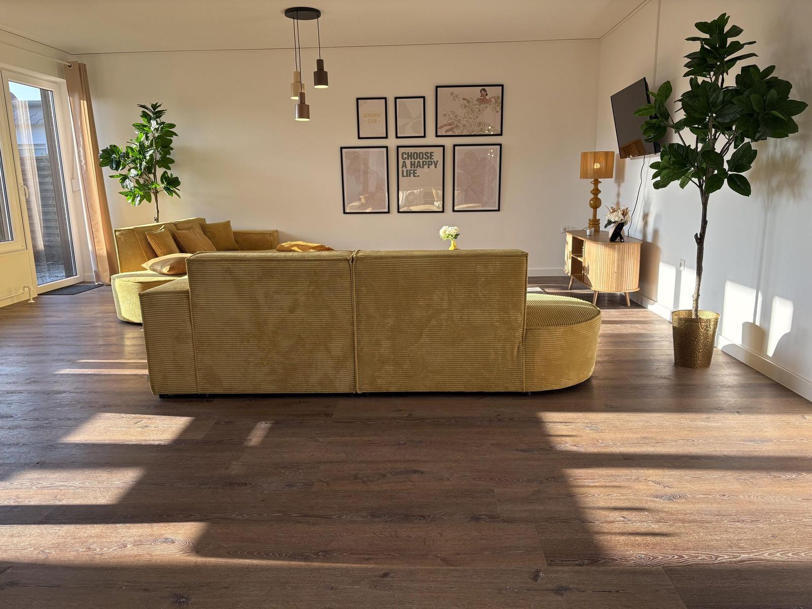 Wohnzimmer mit gelbem Sofa, Holzboden und Wandbildern.