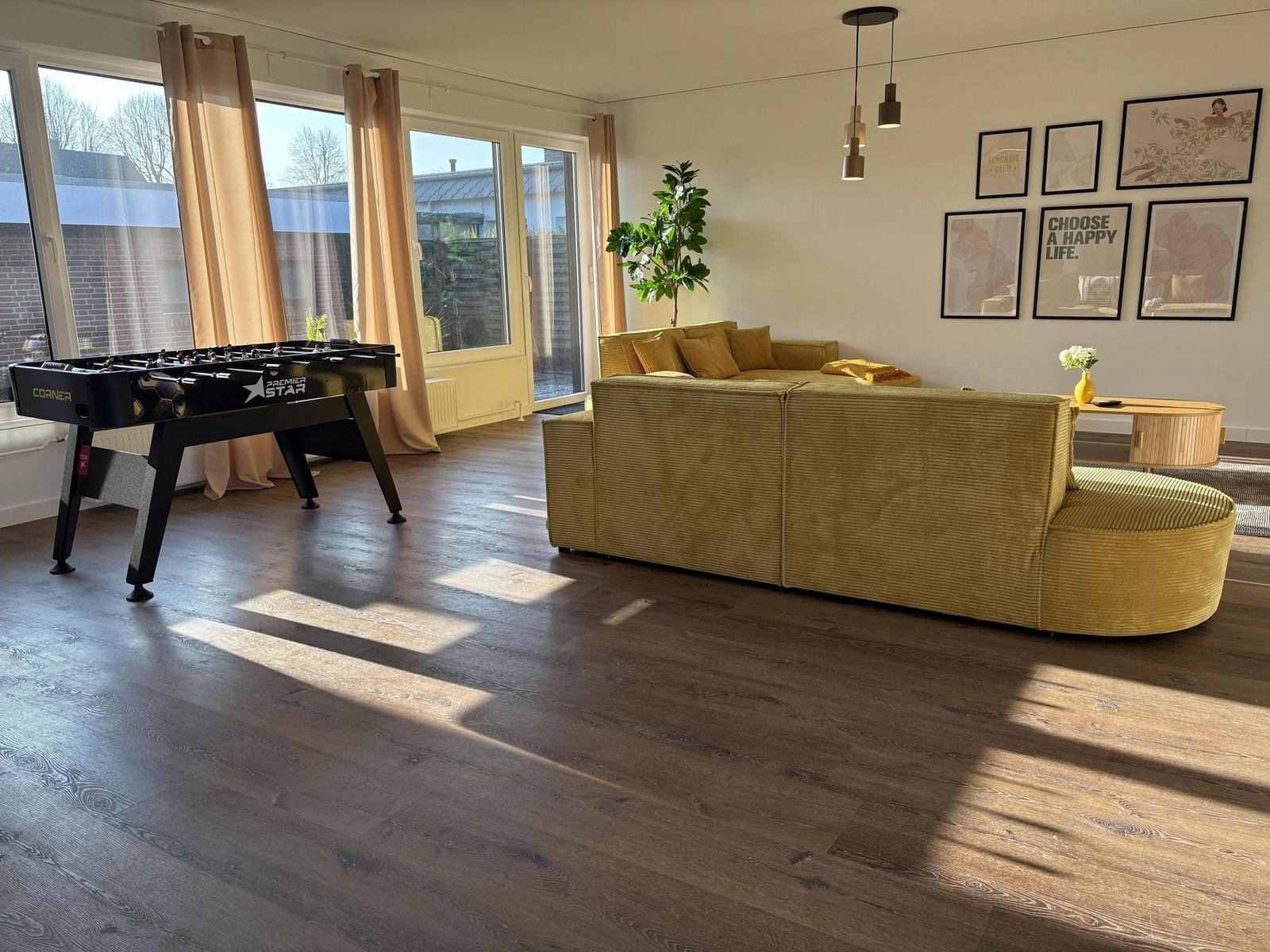 Wohnzimmer mit Sofa, Tischfußball und großen Fenstern.