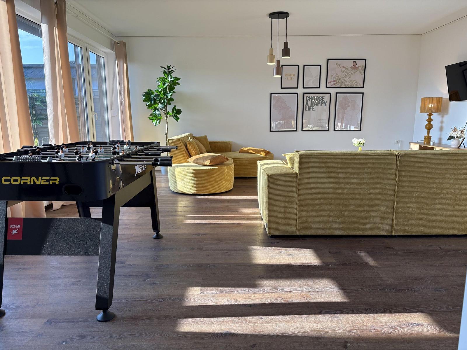 Wohnzimmer mit Sofa, Tischfußball und Pflanze. Wanddekoration und Holzboden.