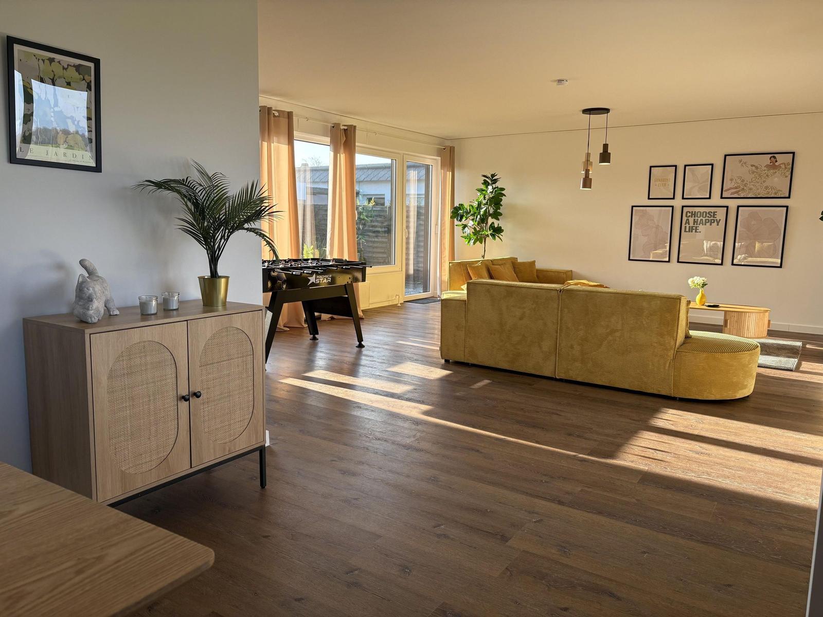 Wohnzimmer mit gelbem Sofa, Holzboden und Fenster zur Terrasse.