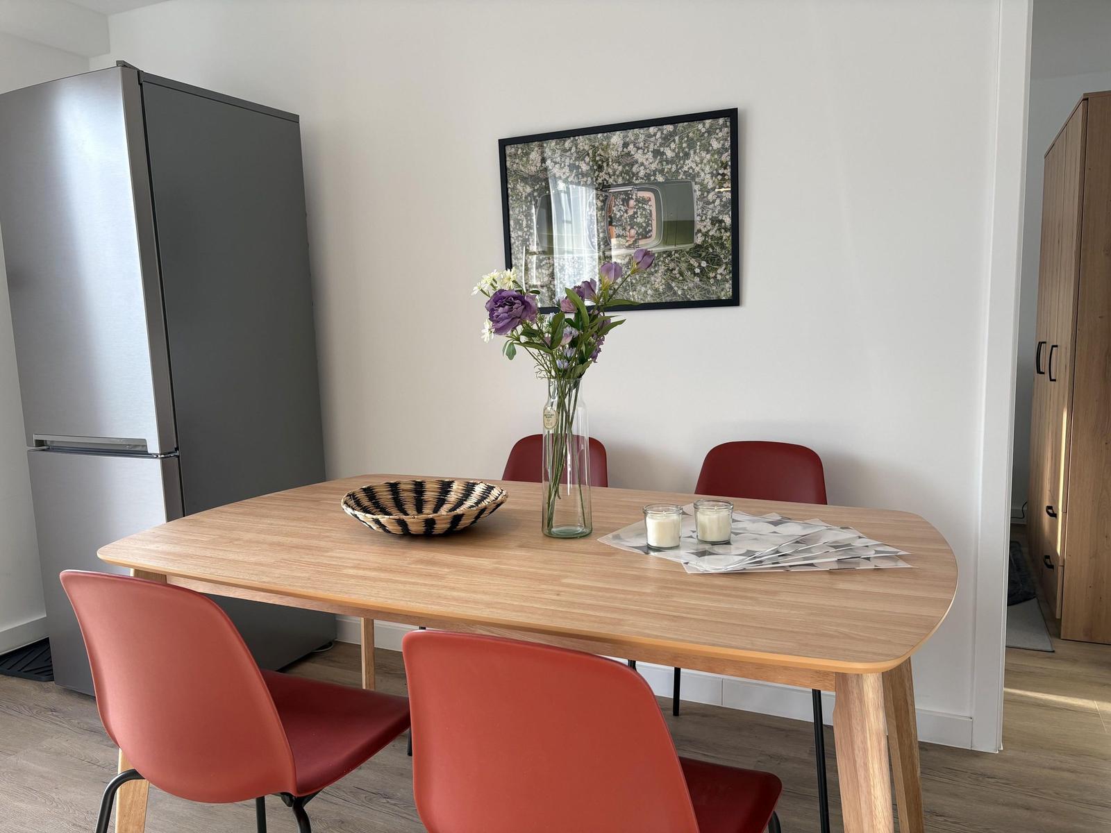 Essbereich mit Holztisch, roten Stühlen und Kühlschrank.