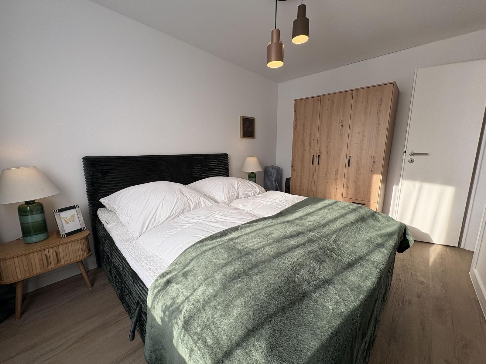 Schlafzimmer mit Doppelbett, Holzschrank und Nachttisch mit Lampe.