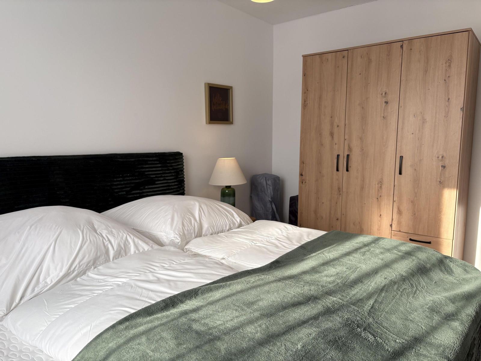 Schlafzimmer mit Bett, Kleiderschrank und Nachttischlampe.