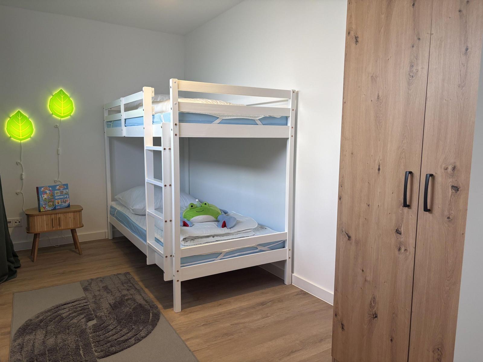 Zimmer mit Doppelstockbett, Kleiderschrank und Wandlampen in Form von Blättern.