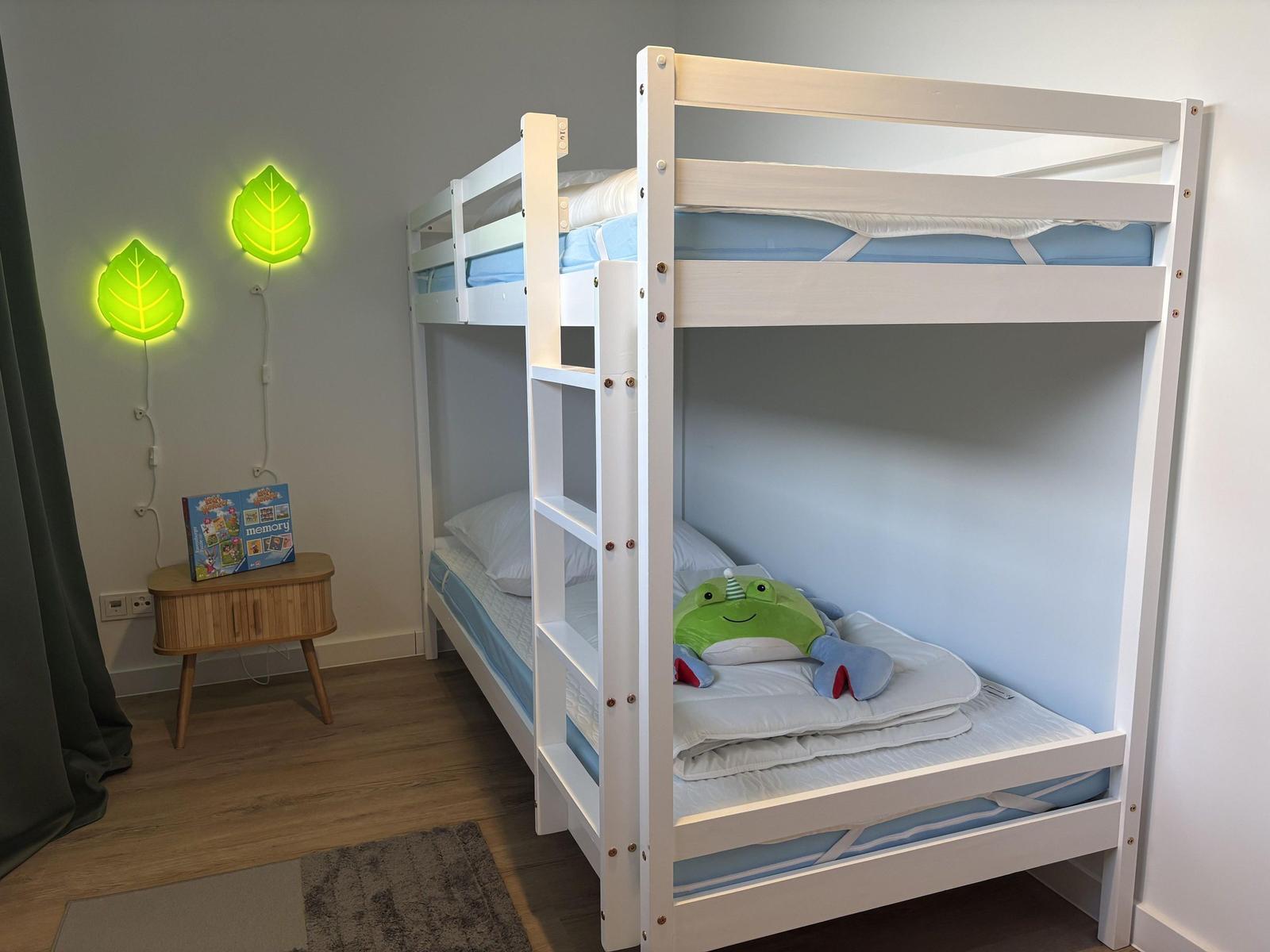Zimmer mit Doppelstockbett, Nachttisch und Wandbeleuchtung in Blätterform.