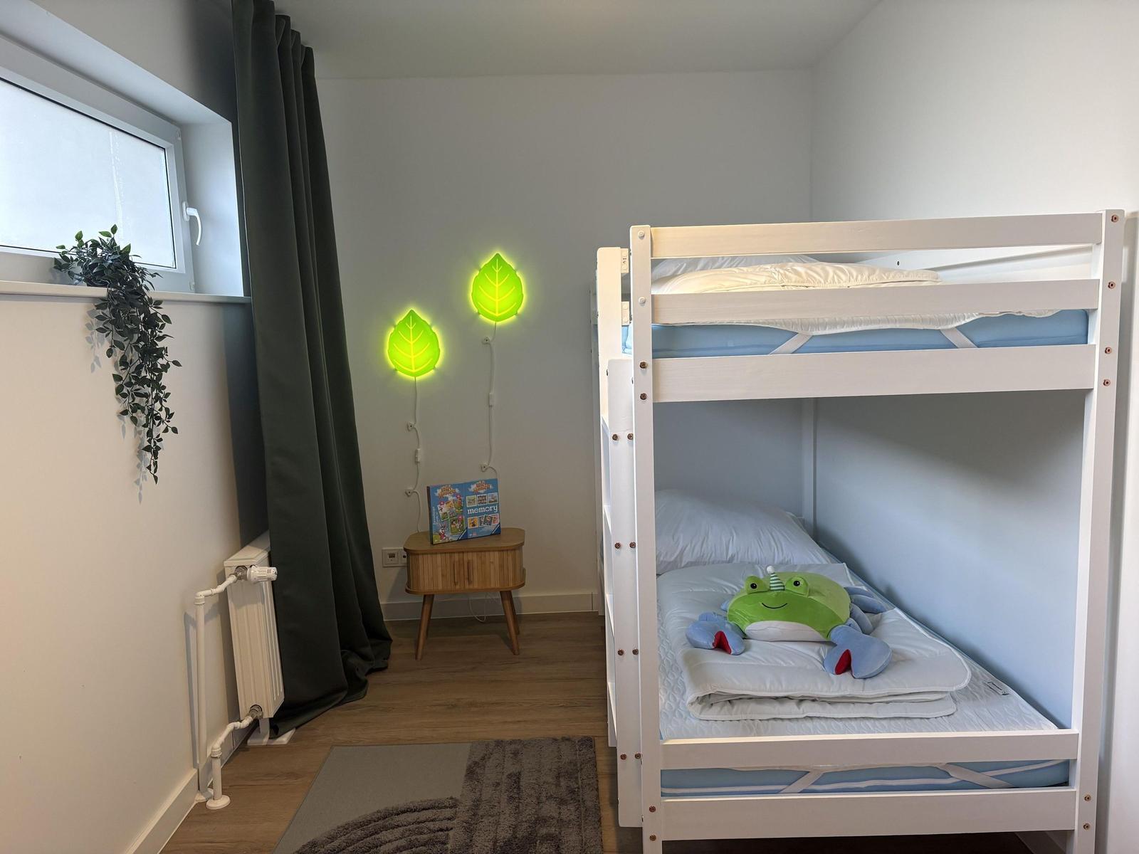 Zimmer mit Doppelbett, Nachttisch und Fenster mit Vorhängen.