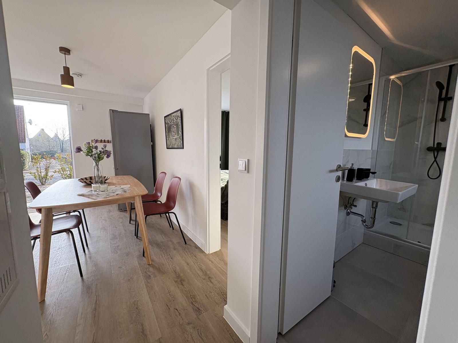 Essbereich mit Tisch und Stühlen, angrenzender Badezimmer mit Dusche und Waschbecken.