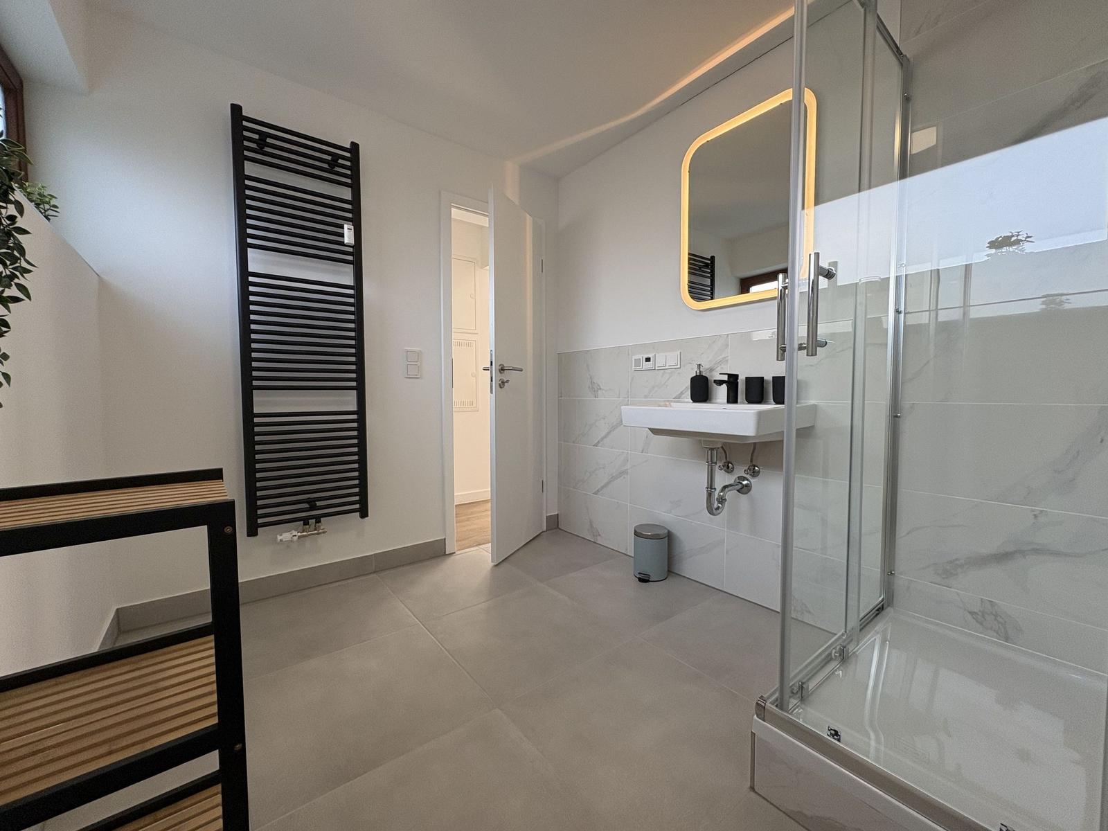 Badezimmer mit Dusche, Waschbecken und Heizkörper.