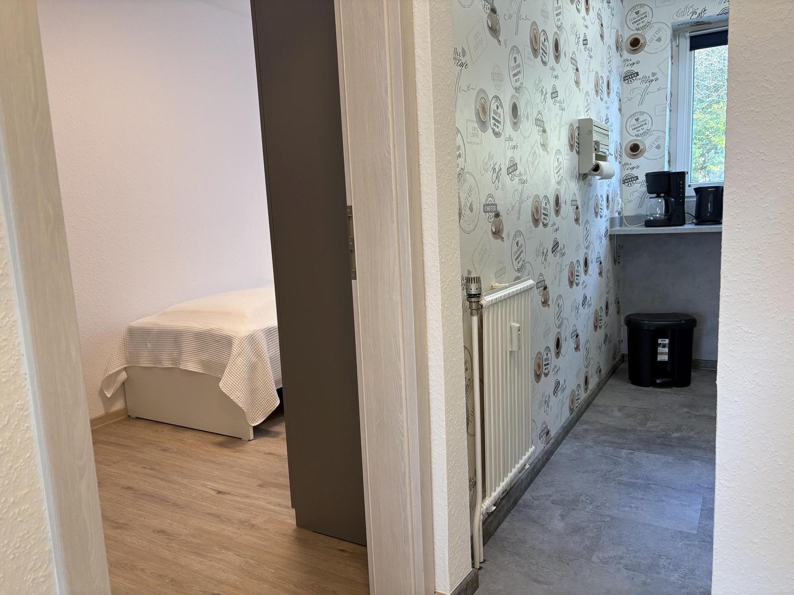 Schlafzimmer mit Bett und angrenzender Küchenzeile mit Kaffeemaschine.