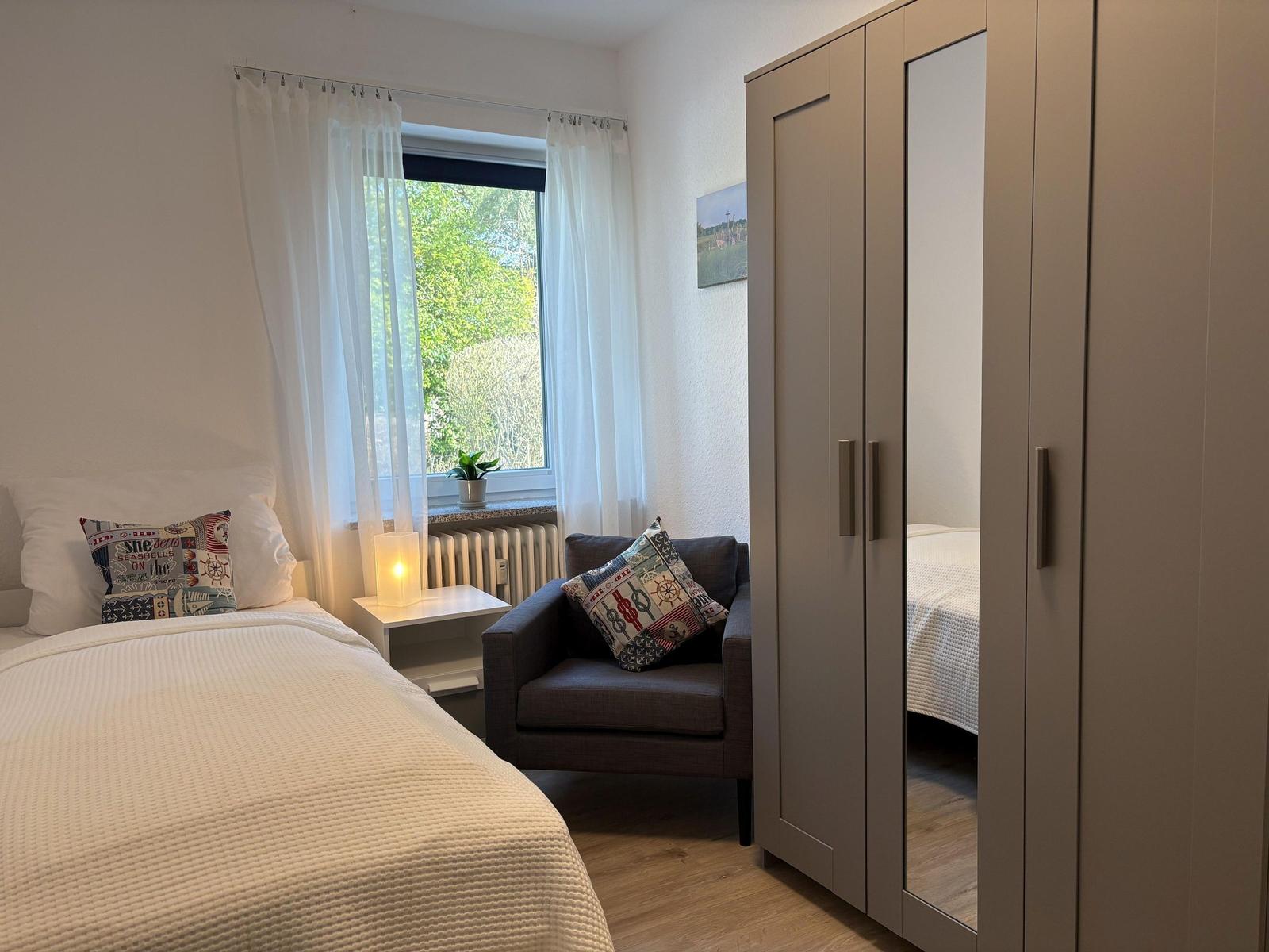 Schlafzimmer mit Bett, Kleiderschrank und Fenster mit Blick auf Grün.