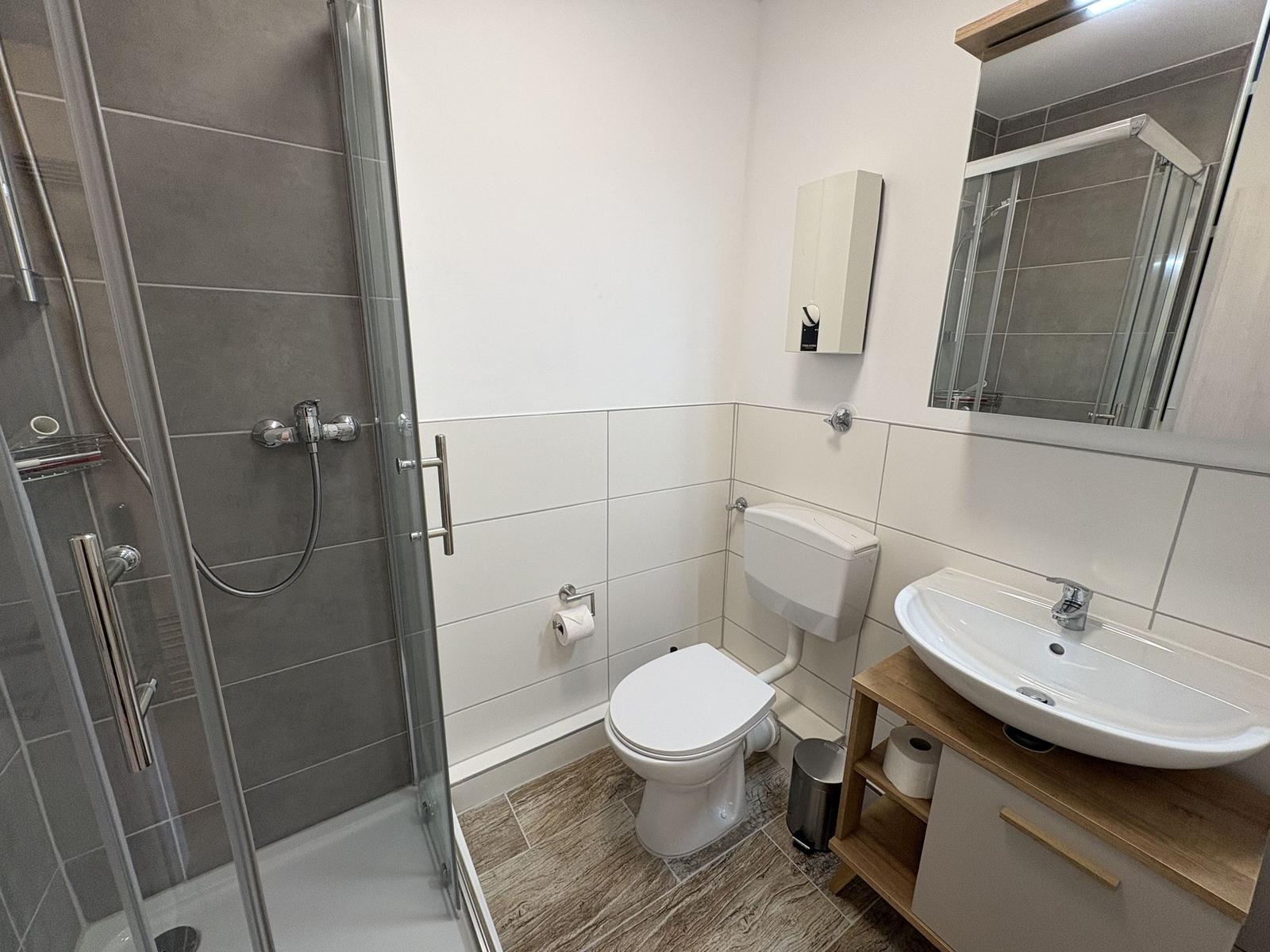 Badezimmer mit Dusche, WC und Waschbecken.