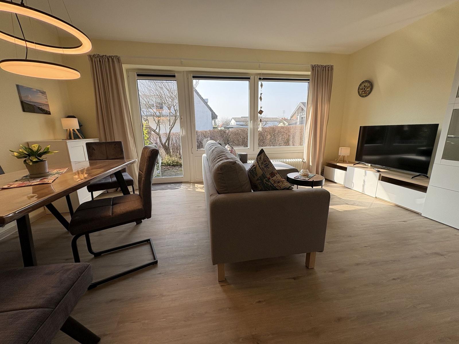 Wohn- und Essbereich mit Sofa, TV und großem Fenster zur Außenterrasse.