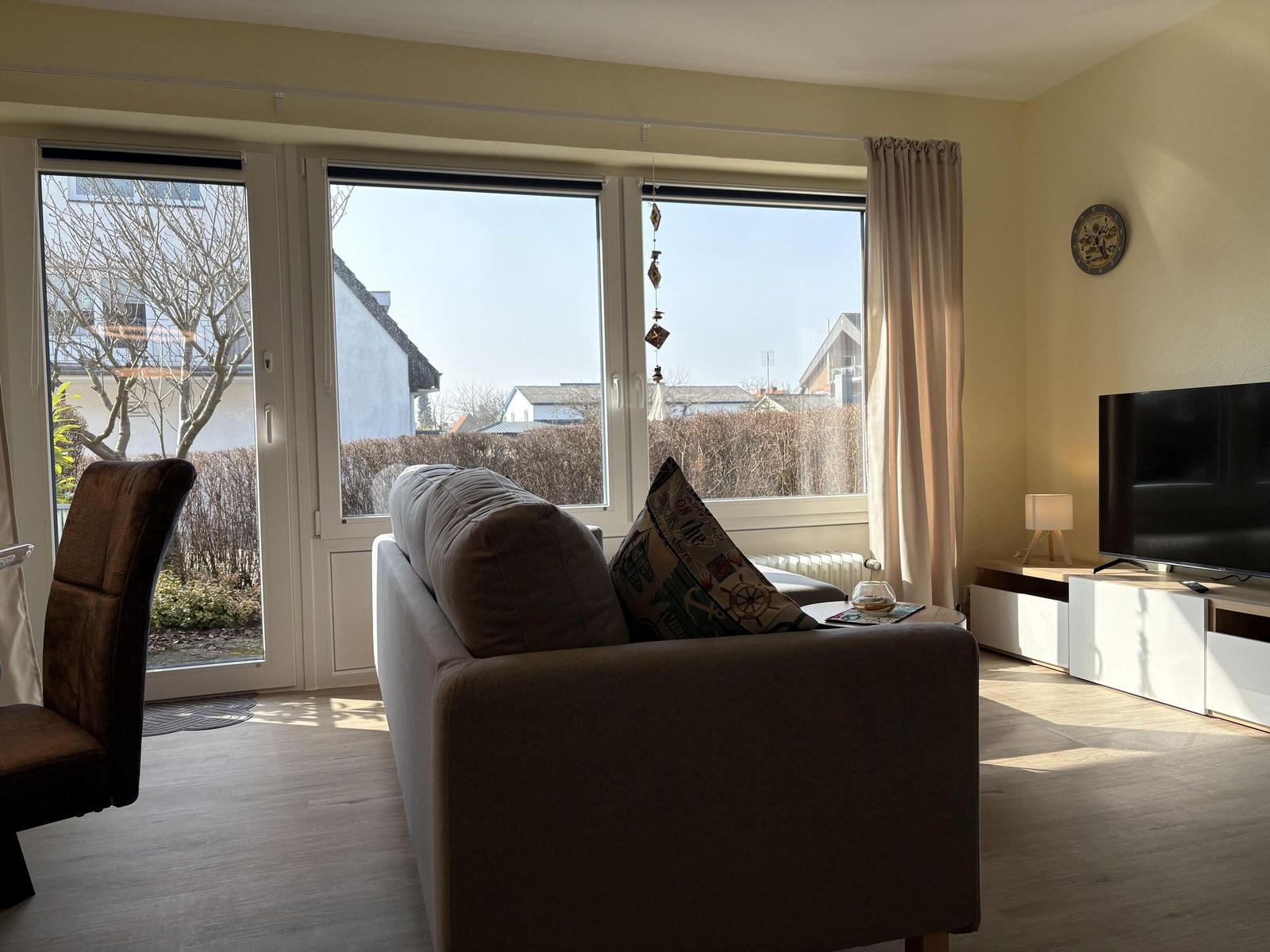 Wohnzimmer mit Sofa, TV und Fenstern zum Garten