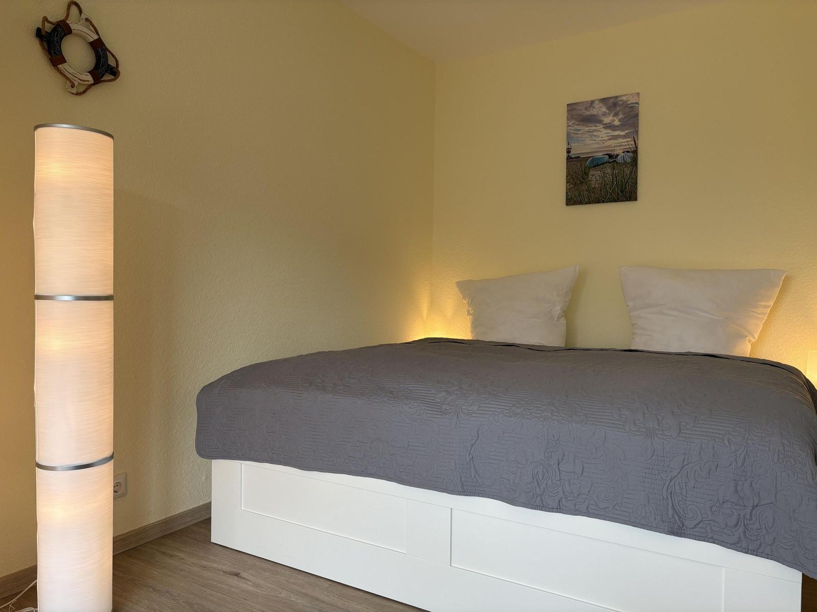 Schlafzimmer mit Bett, Stehlampe und Wandbild