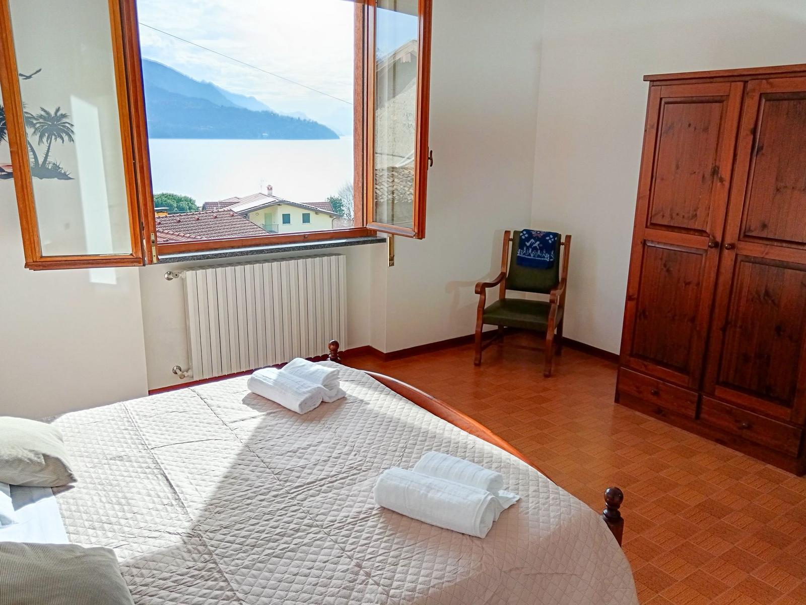 Schlafzimmer mit Blick auf See und Berge. Bett, Stuhl und Schrank sind sichtbar.