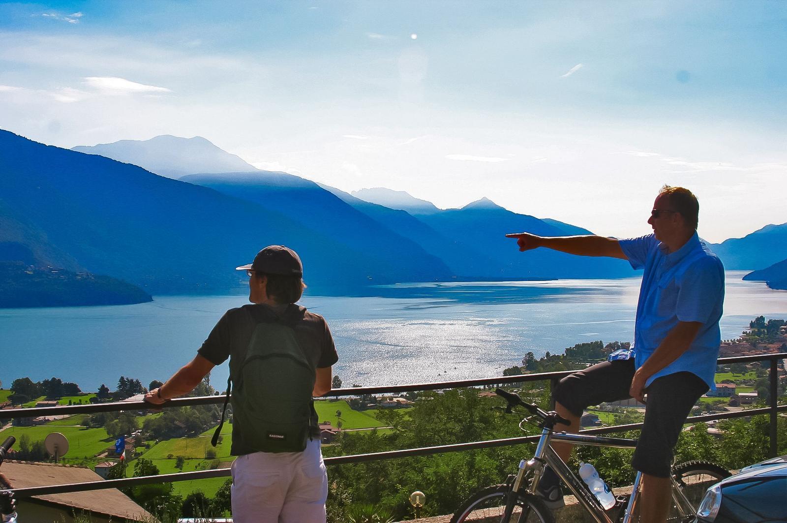Zwei Personen genießen die Aussicht auf See und Berge von einer Terrasse.