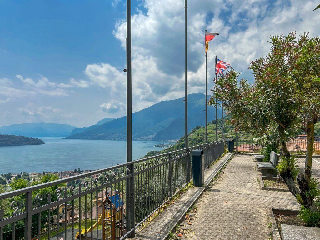 Terrasse mit Blick auf See und Berge, Flaggen und Bäume sichtbar.