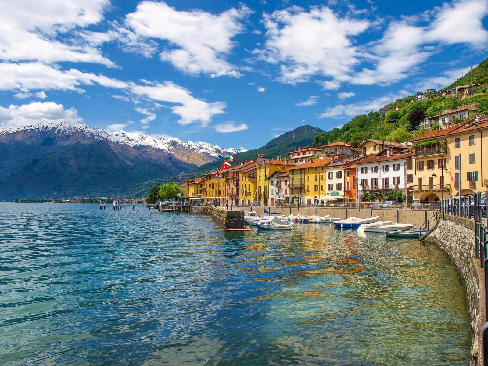 Hafenstadt mit Booten, bunten Häusern und schneebedeckten Bergen im Hintergrund.
