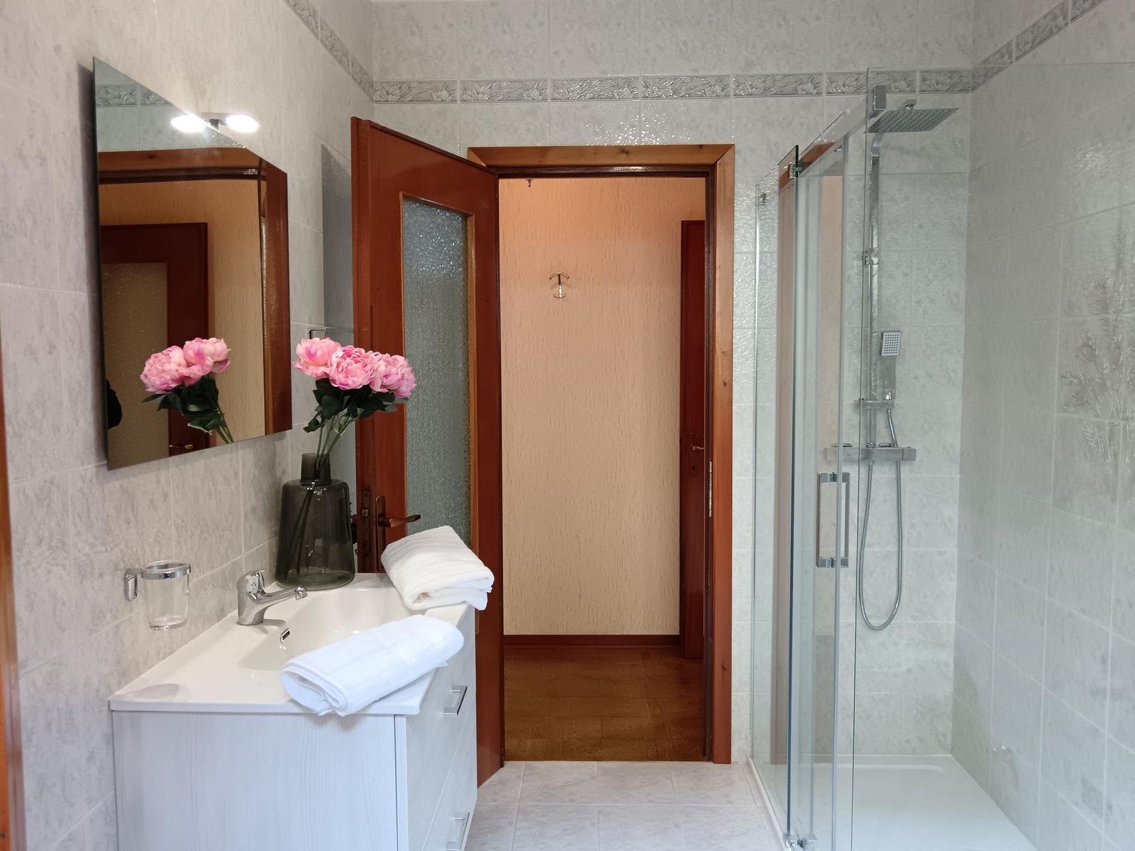 Badezimmer mit Dusche, Waschbecken und Spiegel. Rosa Rosen im Vase.