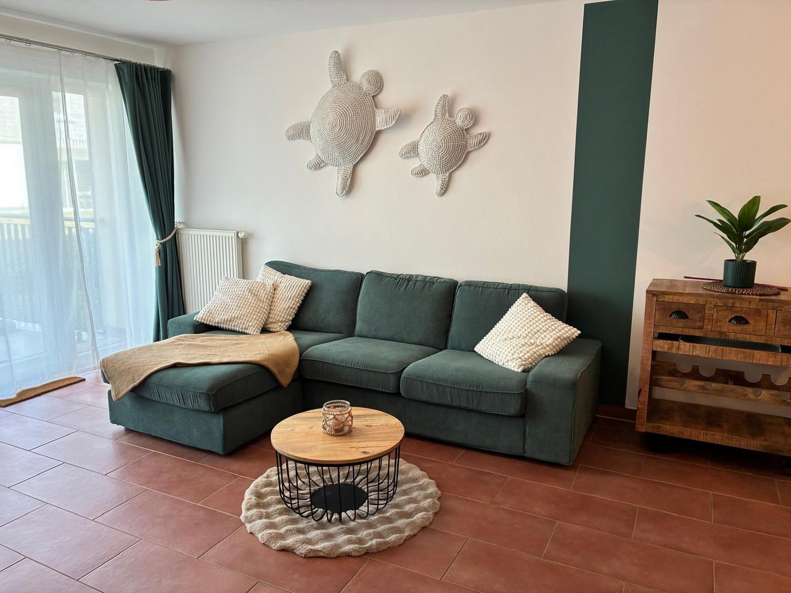 Ein Wohnzimmer mit grünem Sofa, runden Tisch und Wanddekoration.