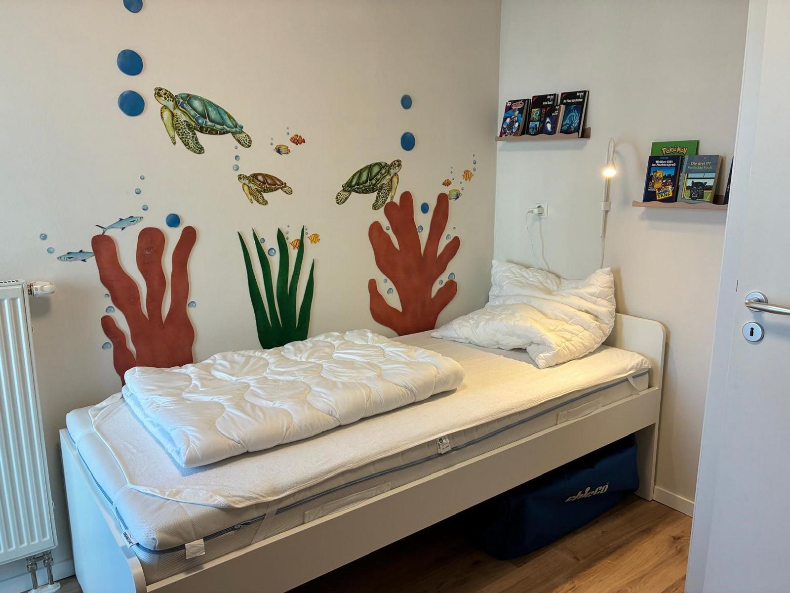 Schlafzimmer mit Unterwasser-Motiv an der Wand und Bett mit weißen Kissen.