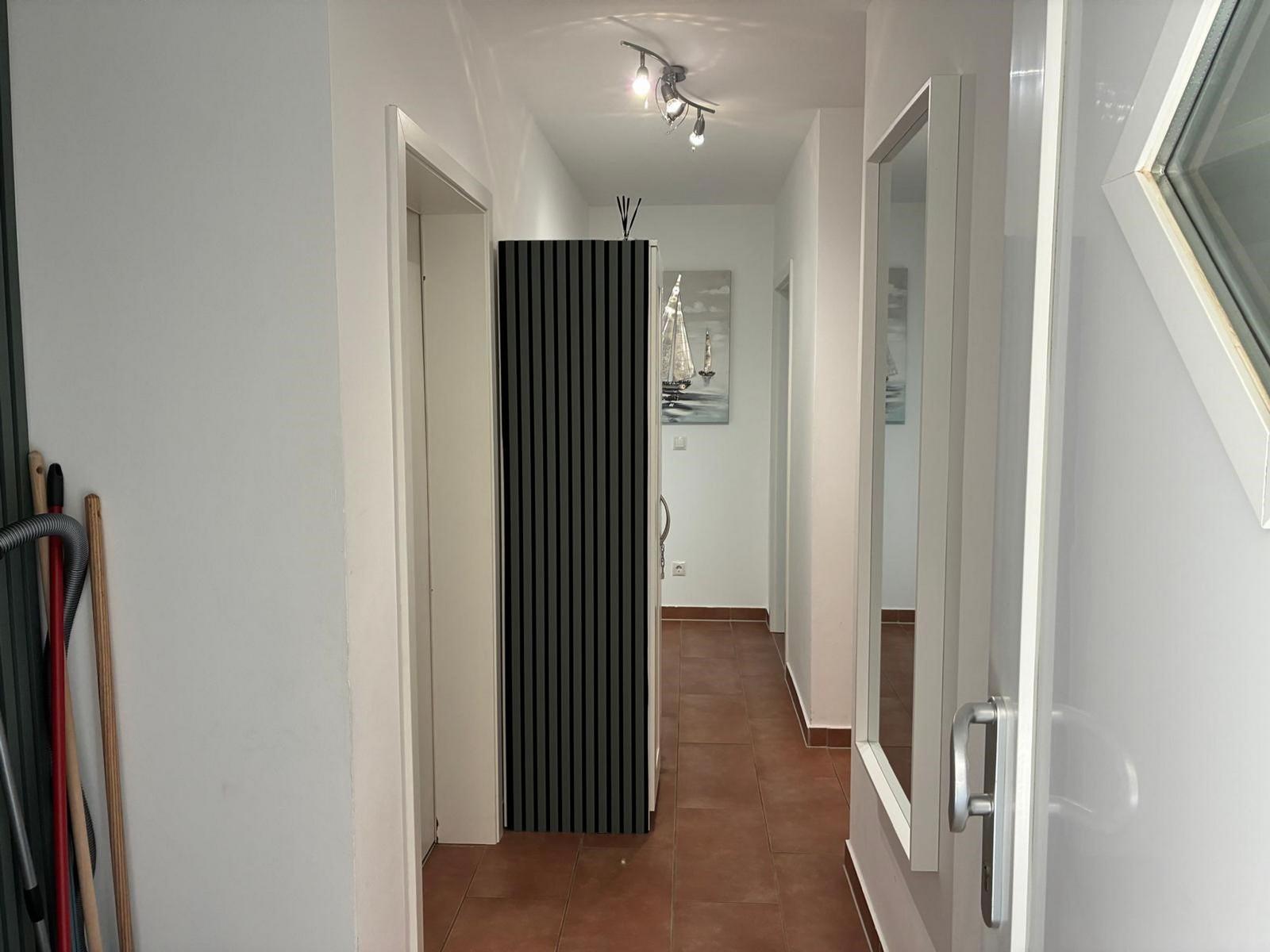 Flur mit braunen Fliesen, schwarzer Garderobe und Wandbild mit Segelbooten.