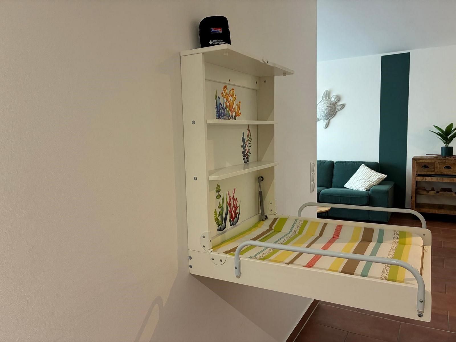 Wandbett mit Regal und Korallenmotiven, dahinter Sofa und Wanddekoration.