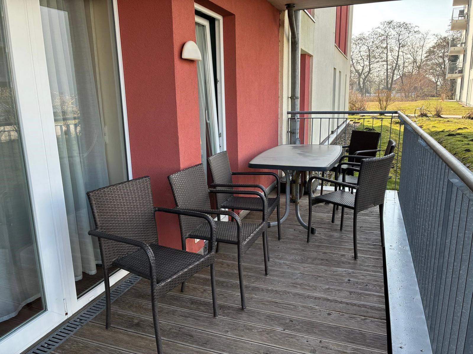 Terrasse mit Tisch und vier Stühlen, Holzboden und roter Wand.