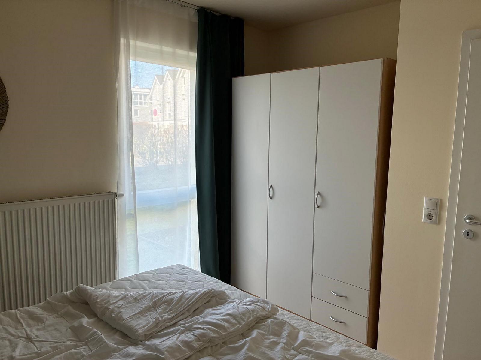 Schlafzimmer mit Bett, Kleiderschrank und Fenster mit Blick auf die Straße.