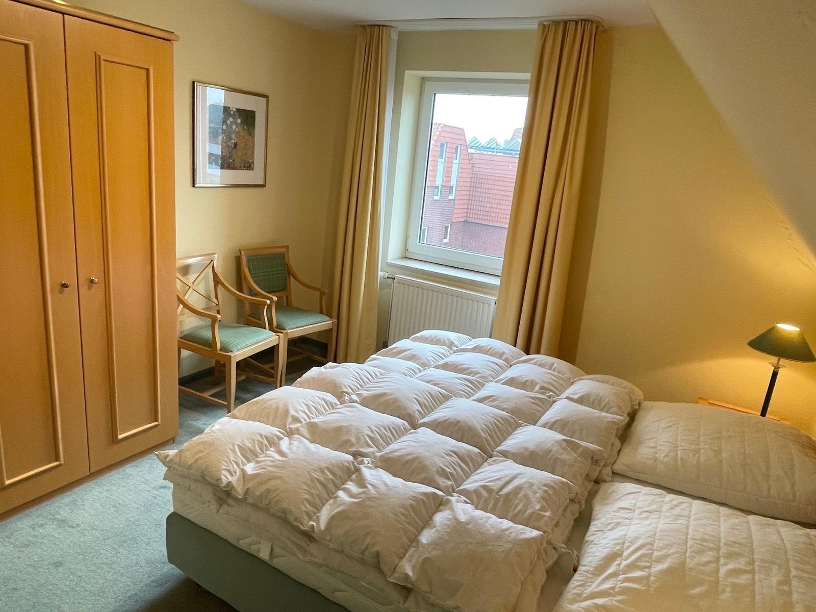 Schlafzimmer mit Doppelbett, Kleiderschrank und Fenster mit Blick auf Dächer.