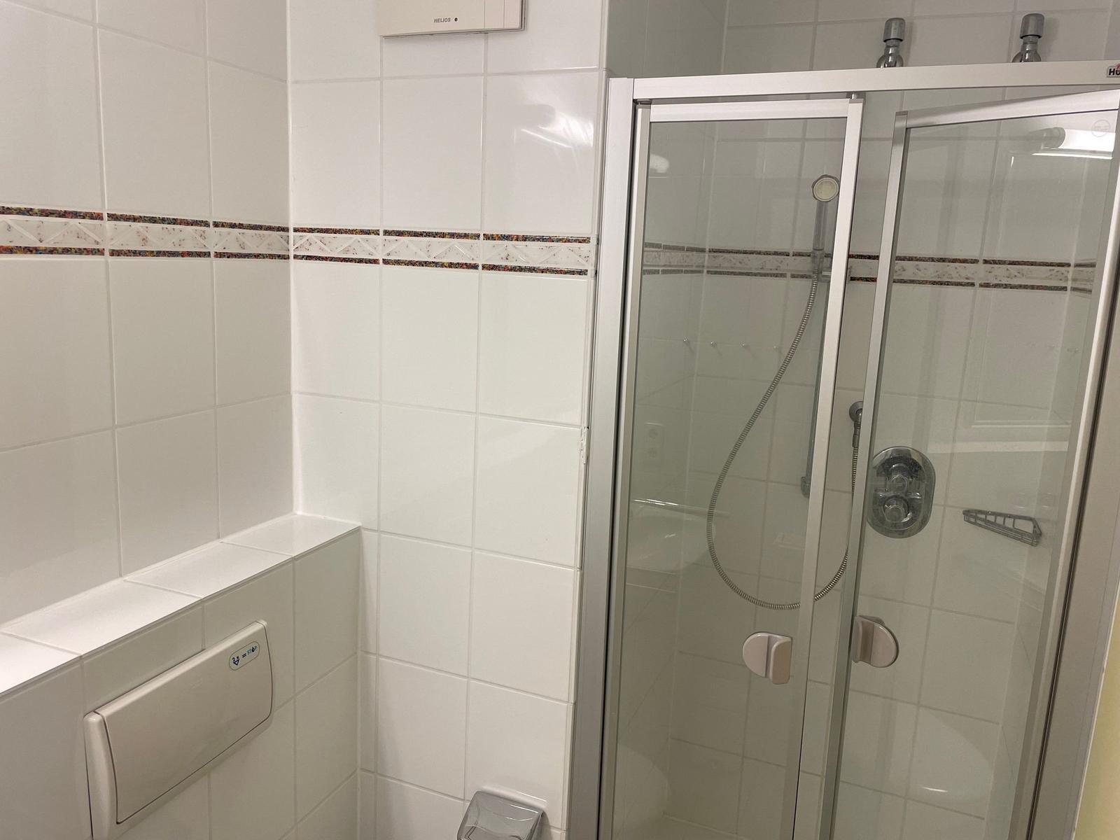 Bad mit Dusche und Toilette. Weiße Fliesen mit dekorativer Bordüre.