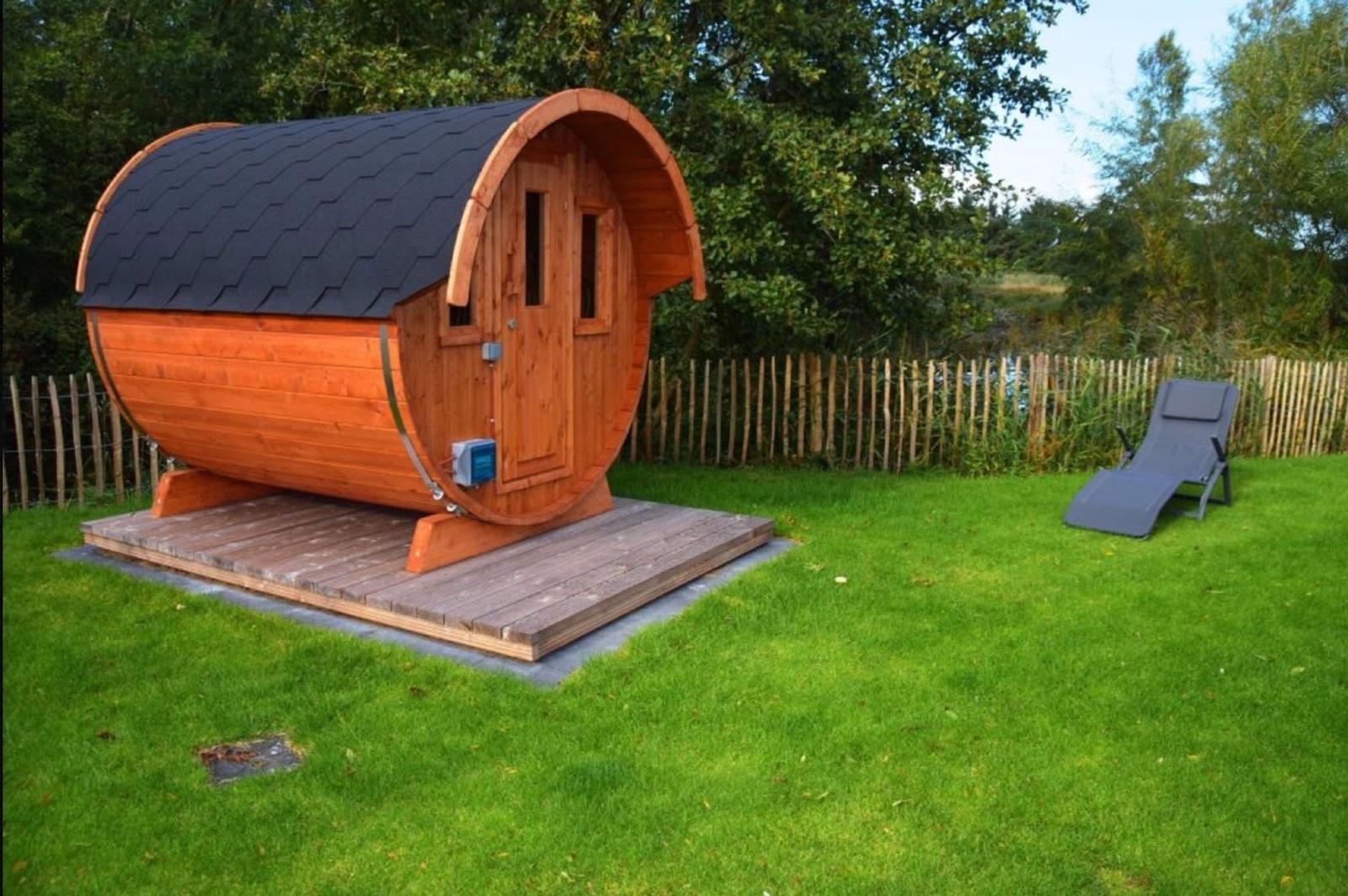 Holzsauna auf Terrasse mit Liegestuhl im Garten.