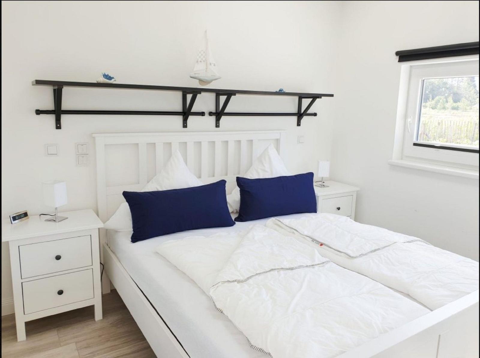 Schlafzimmer mit weißem Bett, Nachttischen und Fenster.
