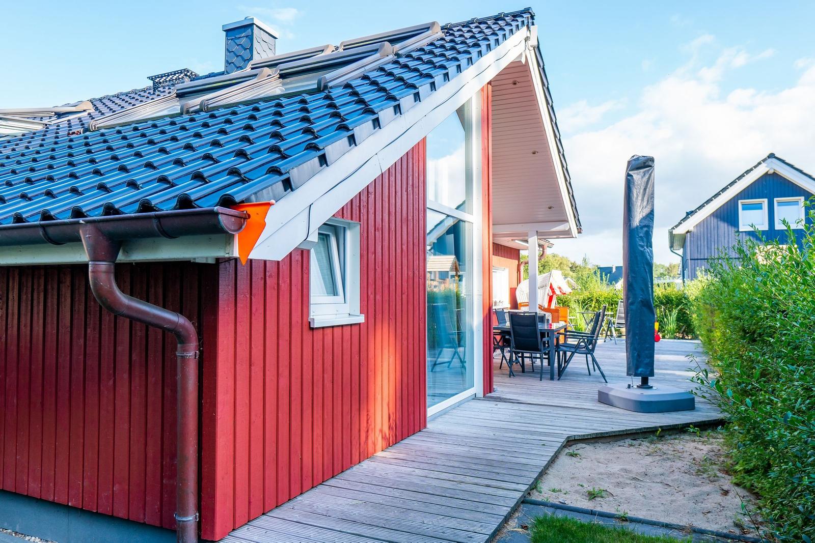 Rotes Holzhaus mit Terrasse und Sitzgelegenheiten.