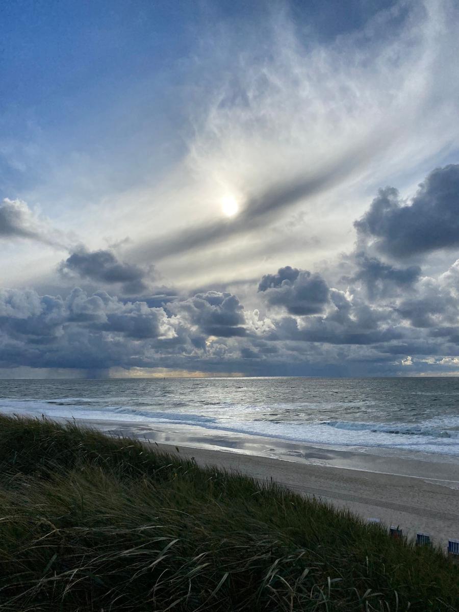 Strand mit Dünen, Meer und bewölktem Himmel mit Sonne.