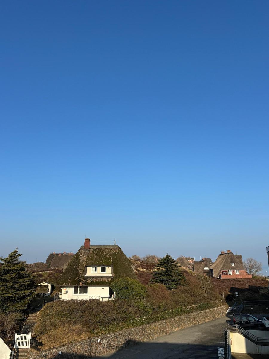 Haus mit strohgedecktem Dach auf grüner Anhöhe unter blauem Himmel.