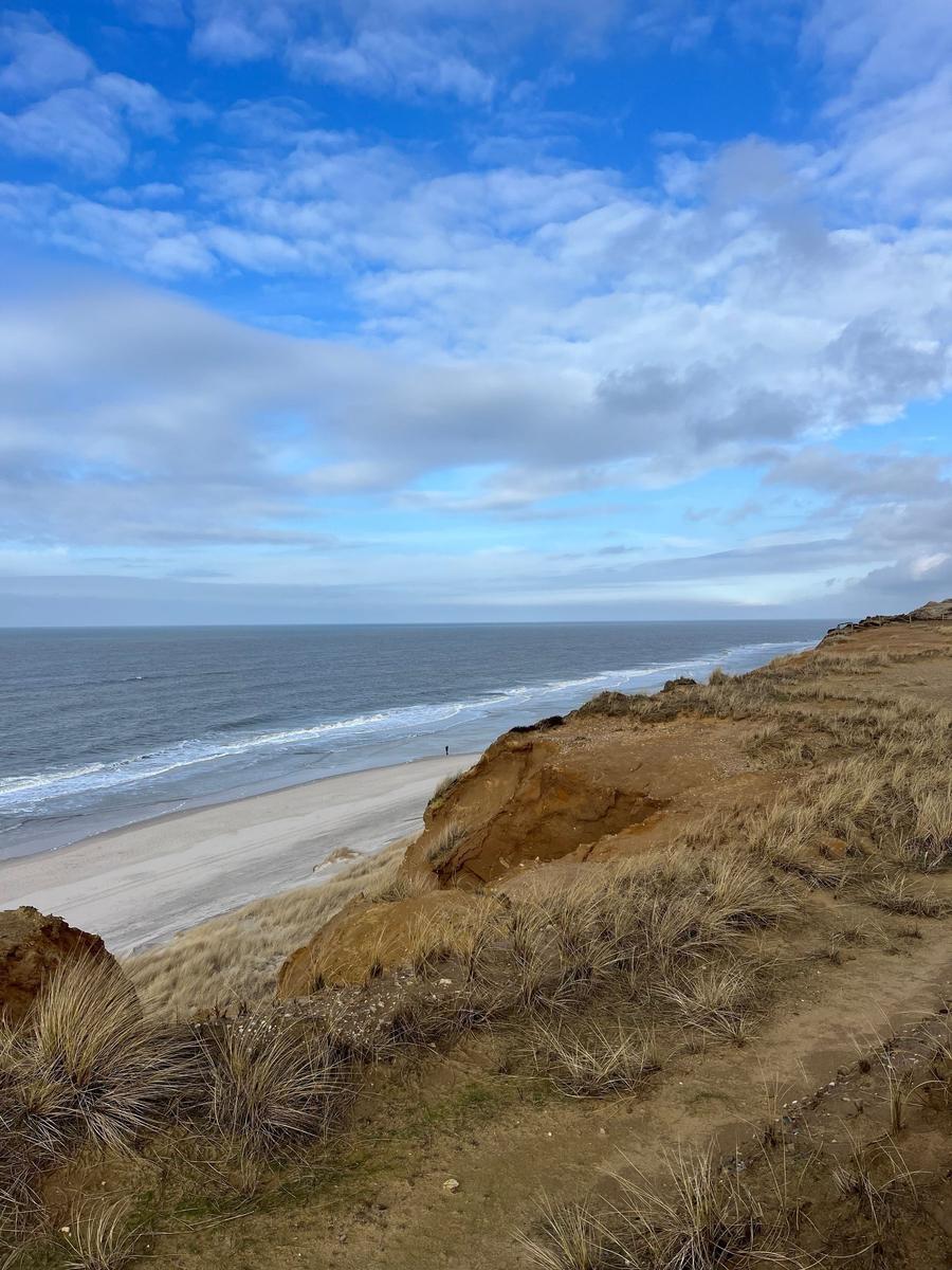 Meer mit Strand und Dünen unter blauem Himmel mit Wolken.
