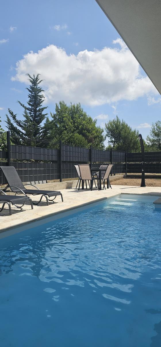 Pool mit Liegen und Tisch im Garten mit Zaun und Bäumen.