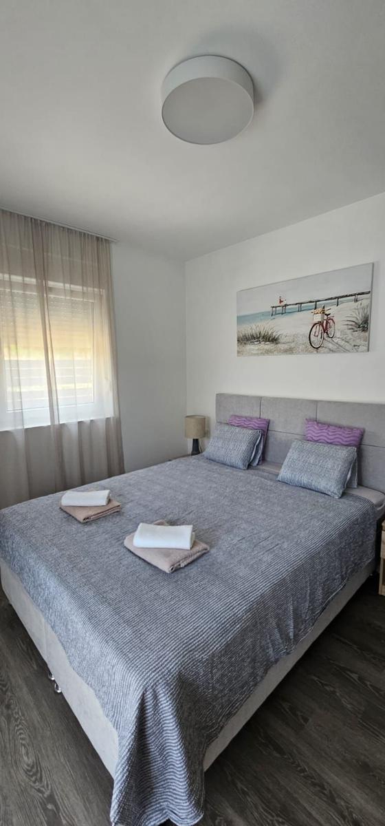 Schlafzimmer mit Doppelbett, Wandbild und Fenster mit Jalousie.