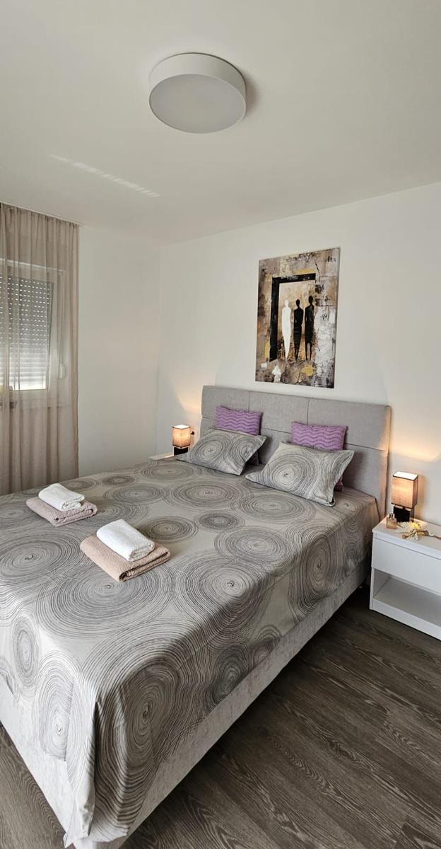 Schlafzimmer mit Doppelbett, Wandbild und zwei Nachttischen mit Lampen.