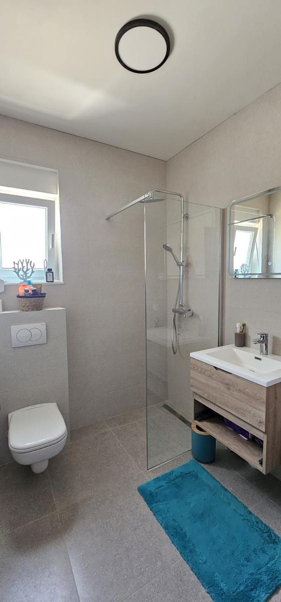 Badezimmer mit Dusche, Waschbecken und Toilette. Blauer Teppich und Spiegel.