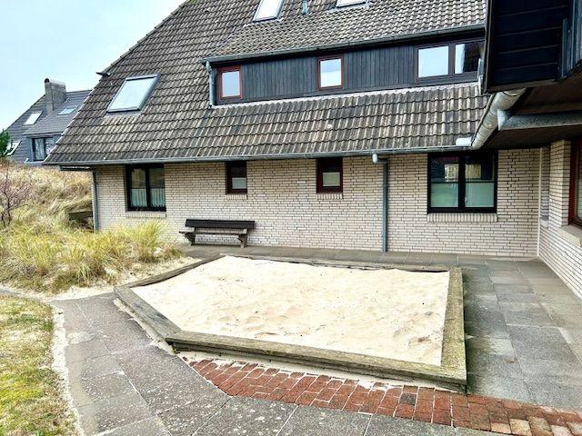 Haus mit Sandkasten und Steinplattenhof. Dach mit Dachfenstern und Ziegeln.