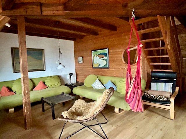 Wohnzimmer mit grünen Sofas, Holzdecke und rotem Hängemattenstuhl.