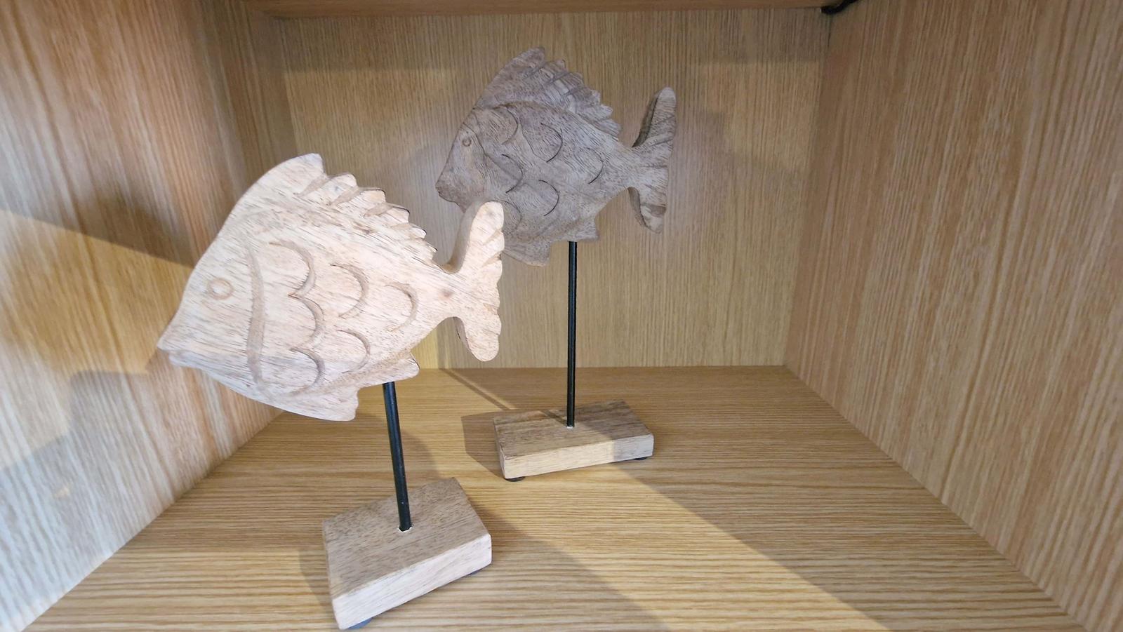 Zwei hölzerne Fischdekorationen auf Ständern in einem Schrank