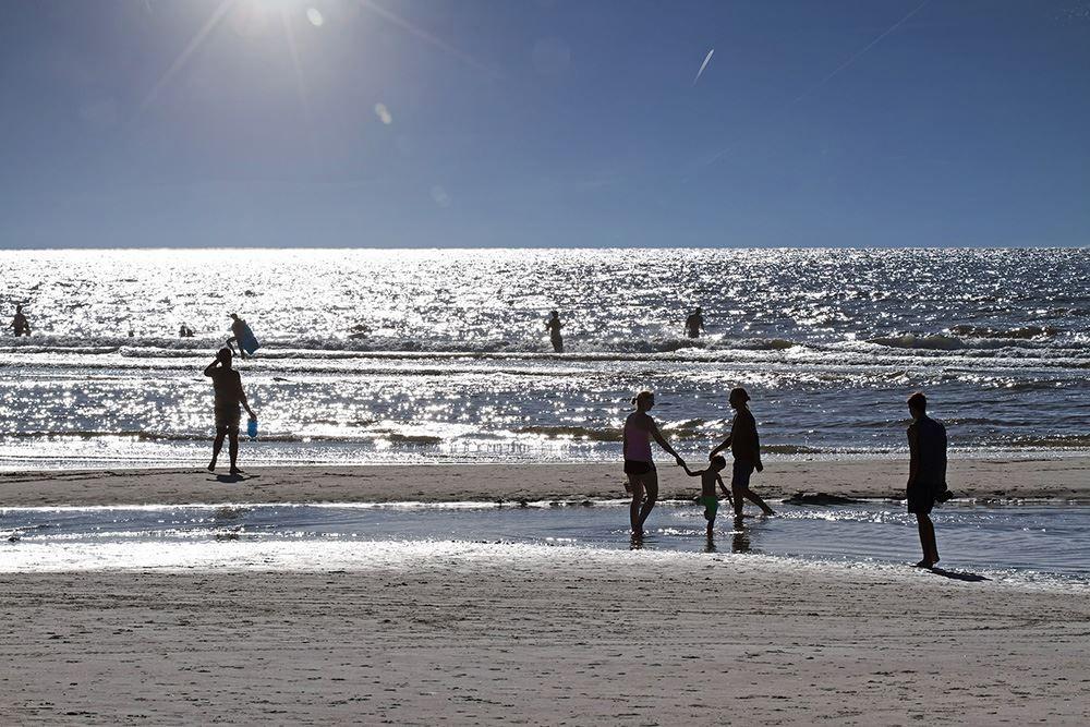 Sonne über dem Meer, Menschen am Strand spazieren und im Wasser spielen.