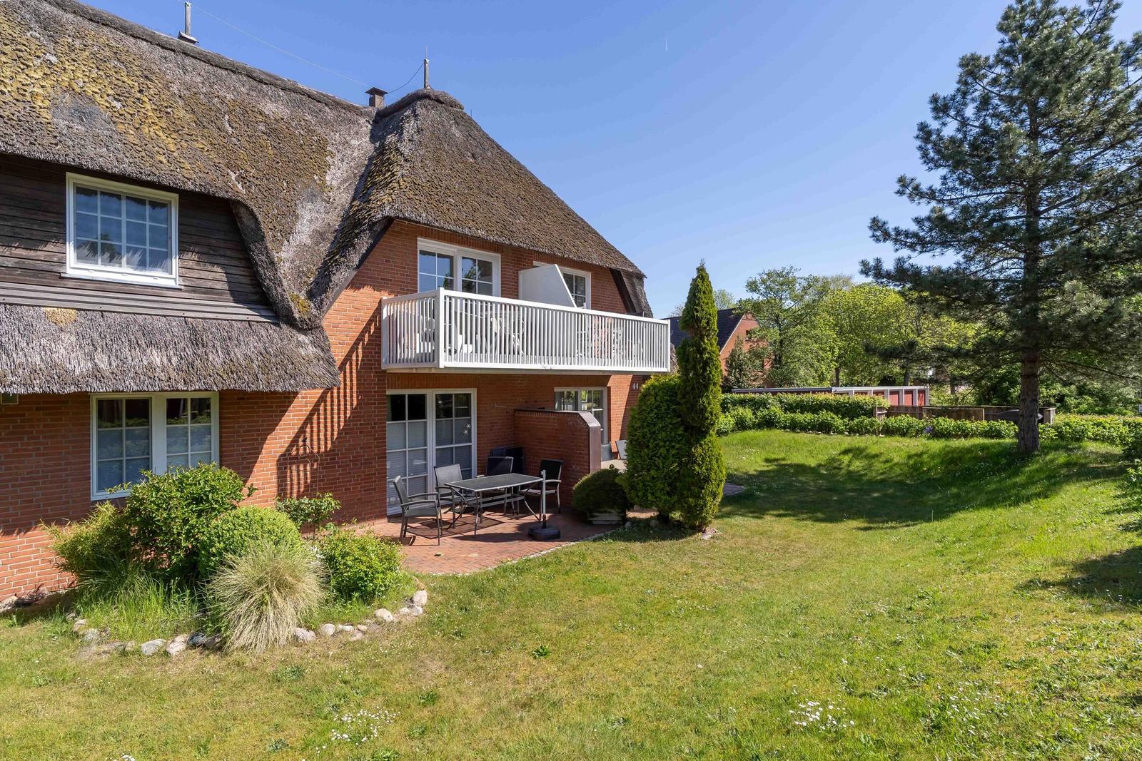 Haus mit Strohdach, Balkon und Garten mit Tisch und Stühlen.