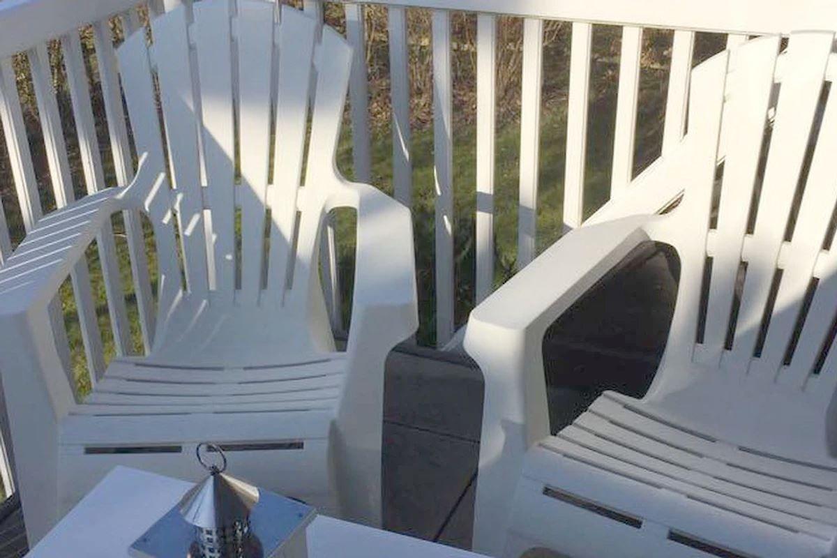 Zwei weiße Sessel und ein Tisch auf einer Terrasse mit Geländer.