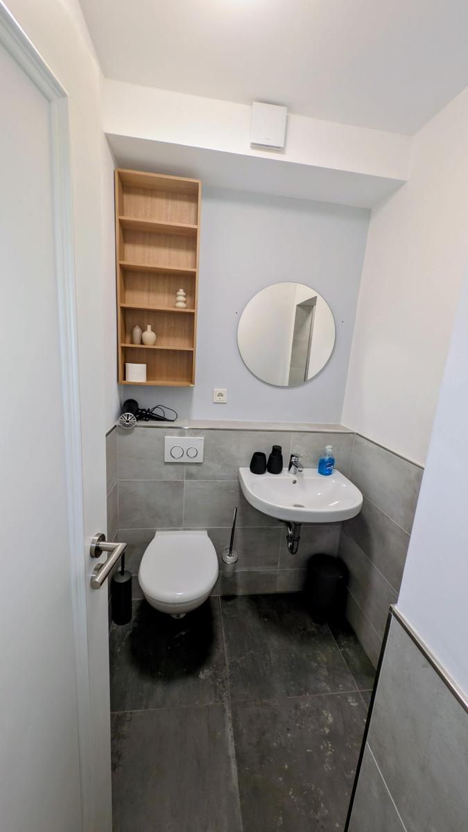 Badezimmer mit Toilette, Waschbecken und Holzregal an der Wand.